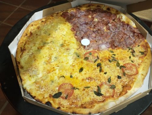 Foto de uma pizza grande de três sabores (muzzarela, calabresa e marguerita) dentro de uma caixa de pizza ocupando todo o espaço da foto.